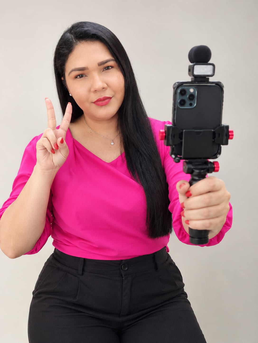 Andreza Campos, video maker mobile e fotógrafa, segurando um celular em suporte com a mão levantada fazendo um sinal de paz