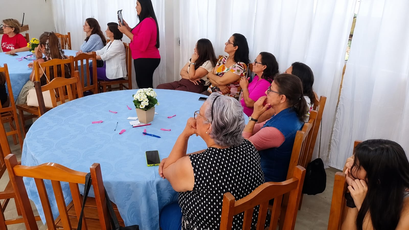 Participantes sentadas nas mesas acompanhando a fala da organizadora