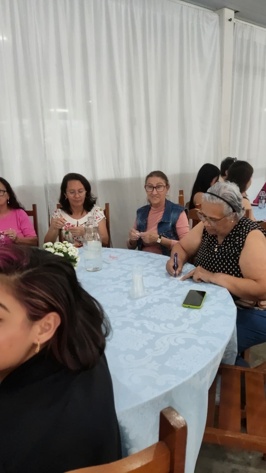 Convidadas sentadas à mesa escrevendo em bilhetes durante a dinâmica