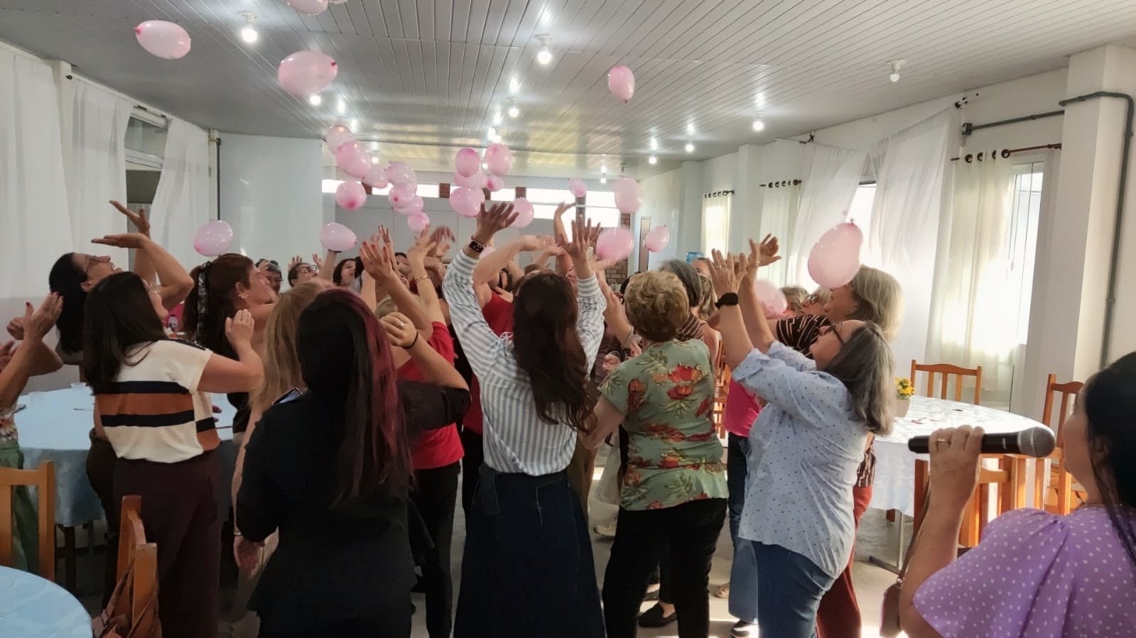Participantes levantando as mãos e jogando balões rosa para o alto