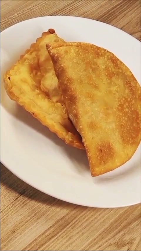Salgados fritos dourados servidos em prato branco sobre mesa de madeira